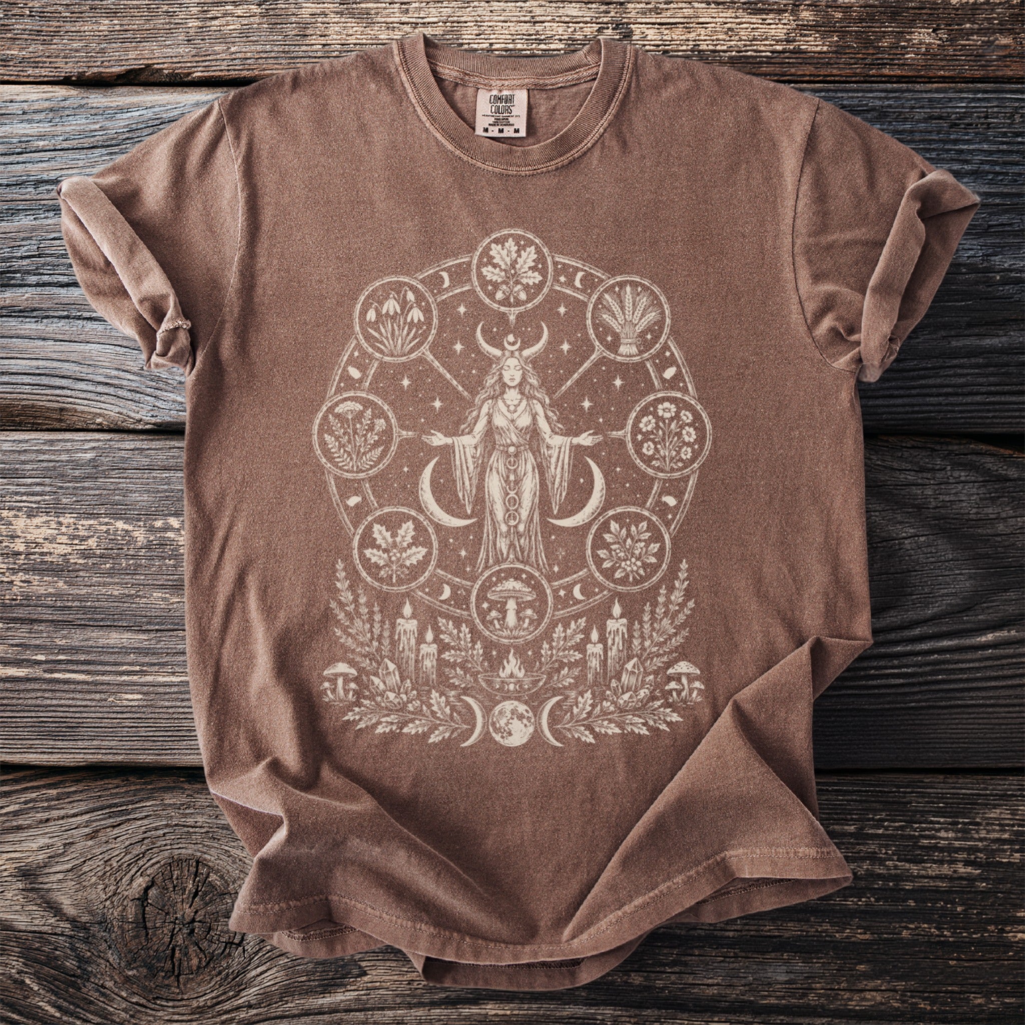 Brown t-shirt with a cream circle design featuring a moon-horned woman and symbols of nature.