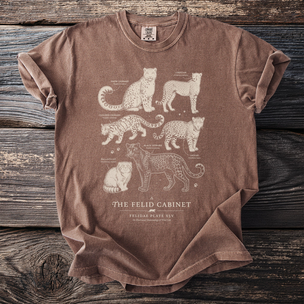 Brown t-shirt featuring illustrations of snow leopard, cheetah, clouded leopard, black leopard, jaguar, and Pallas's cat.