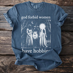 T-shirt with three figures, a broom, lantern, and text "god forbid women have hobbies".