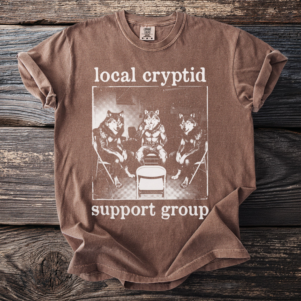 Brown t-shirt with "local cryptid support group" text and graphic of wolves.