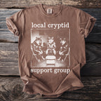 Brown t-shirt with "local cryptid support group" text and graphic of wolves.