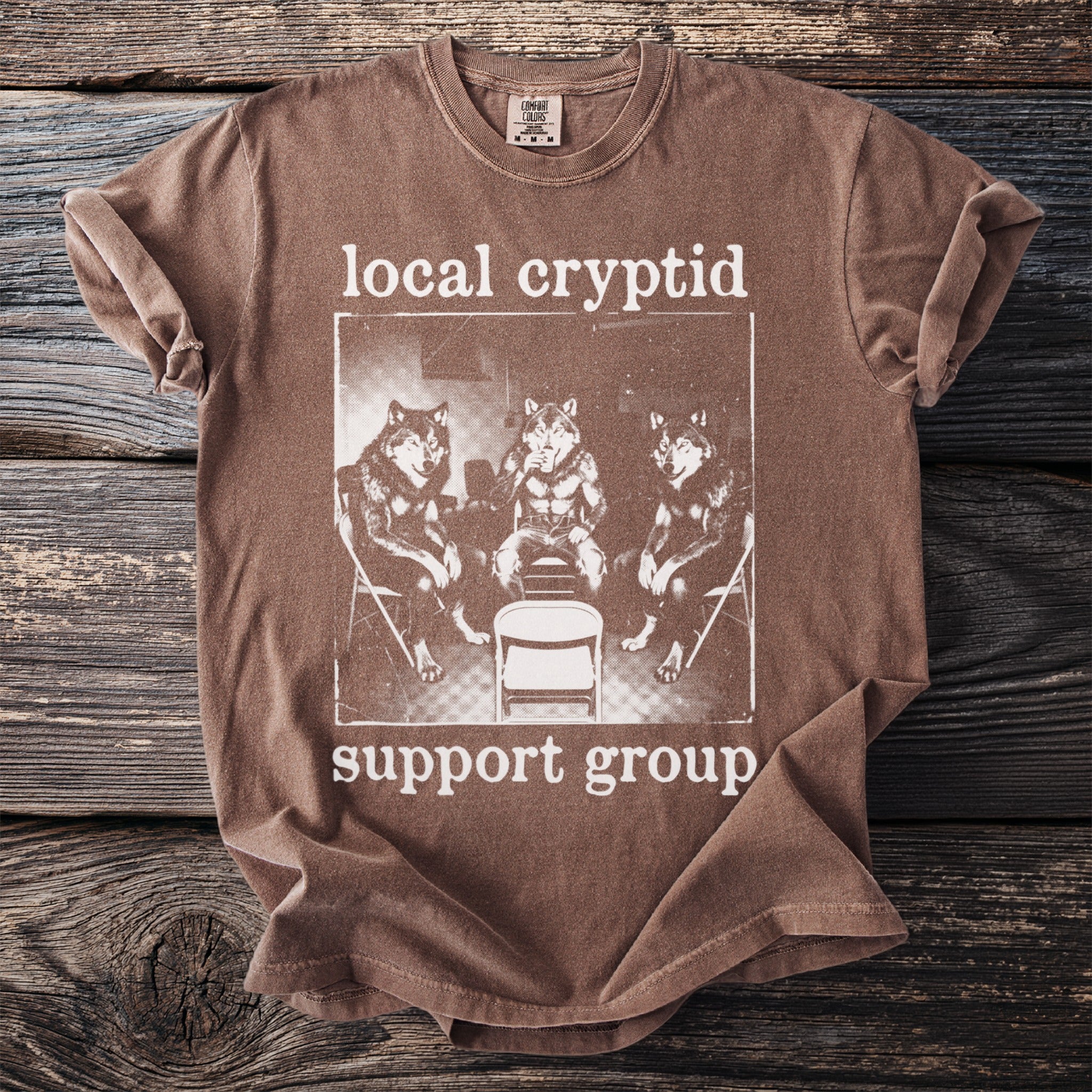 Brown t-shirt with "local cryptid support group" text and graphic of wolves.