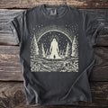 Dark grey t-shirt with a cream graphic of a cryptid in a forest beside a lake.