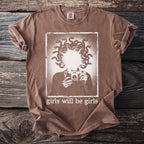 Brown t-shirt with graphic of person holding camera and snakes for hair, text "girls will be girls".