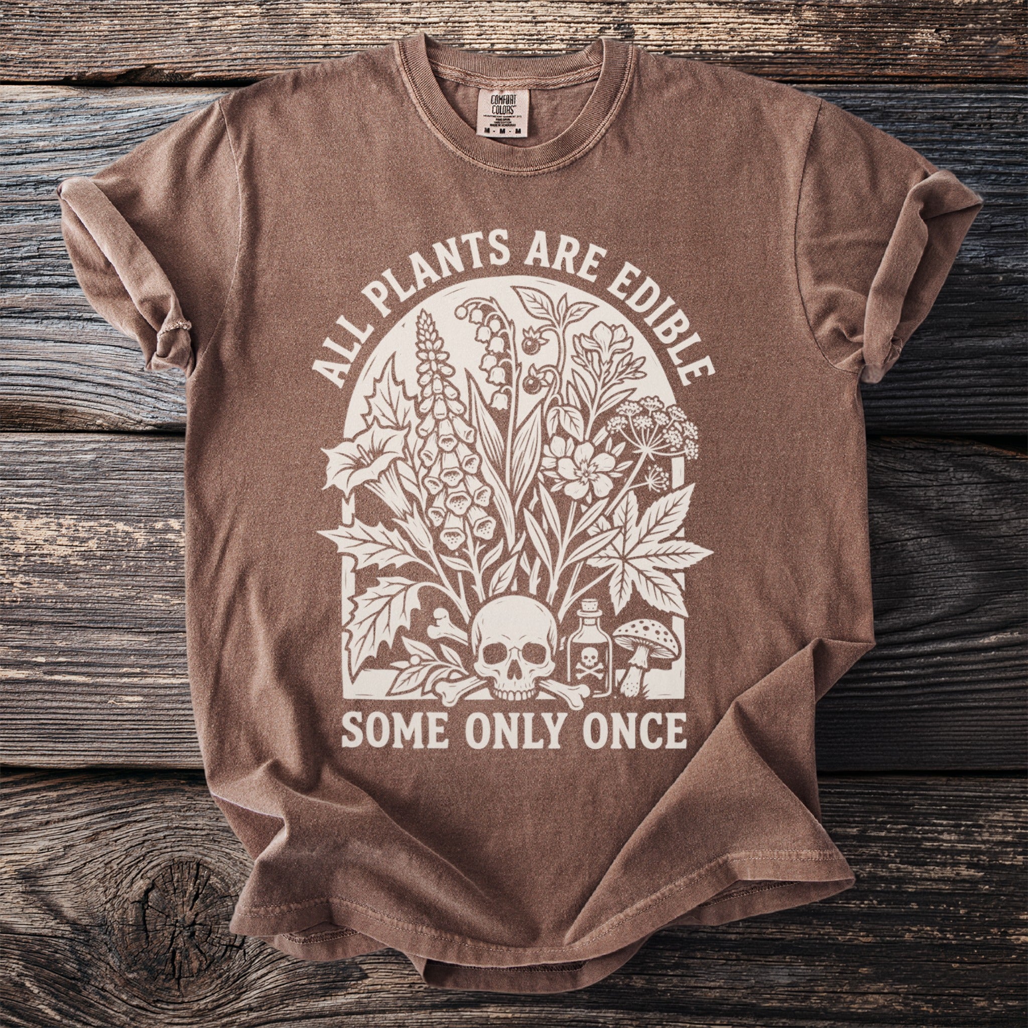 Brown t-shirt with cream graphic featuring plants, skull, poison bottle, and text.