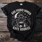 Black t-shirt with white graphic of three cats around a cauldron, text reads "God Forbid Women Have Hobbies".