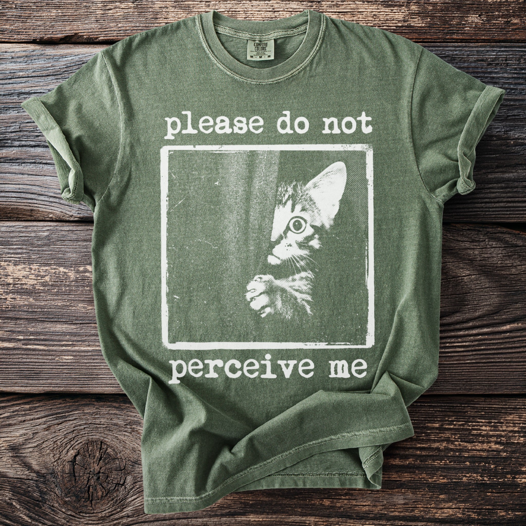 Green t-shirt with a distressed graphic of a cat peering out with text "please do not perceive me".