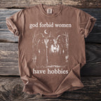 Brown t-shirt with "god forbid women have hobbies" and illustration of witches.