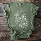 Green t-shirt with a white line drawing of a witch holding mandrake and black henbane.