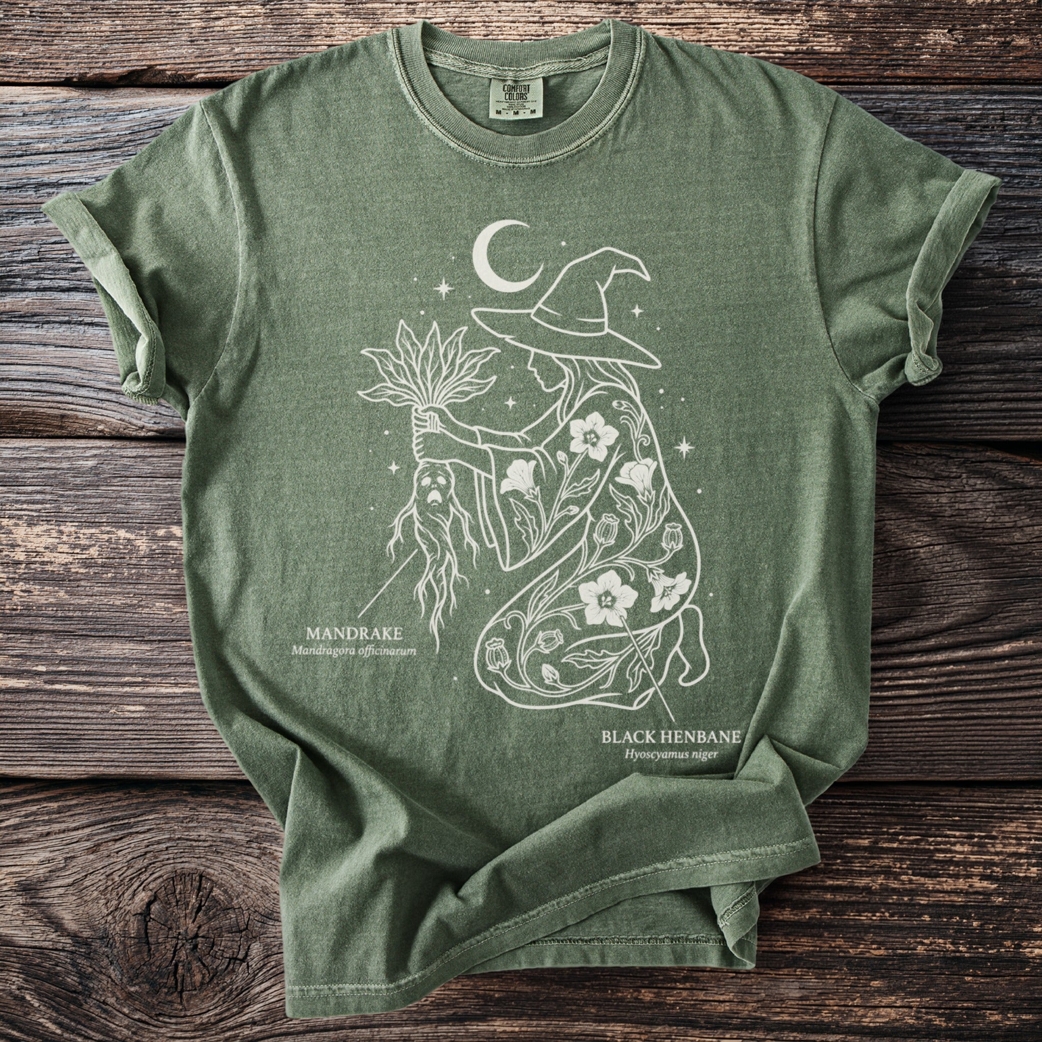 Green t-shirt with a white line drawing of a witch holding mandrake and black henbane.