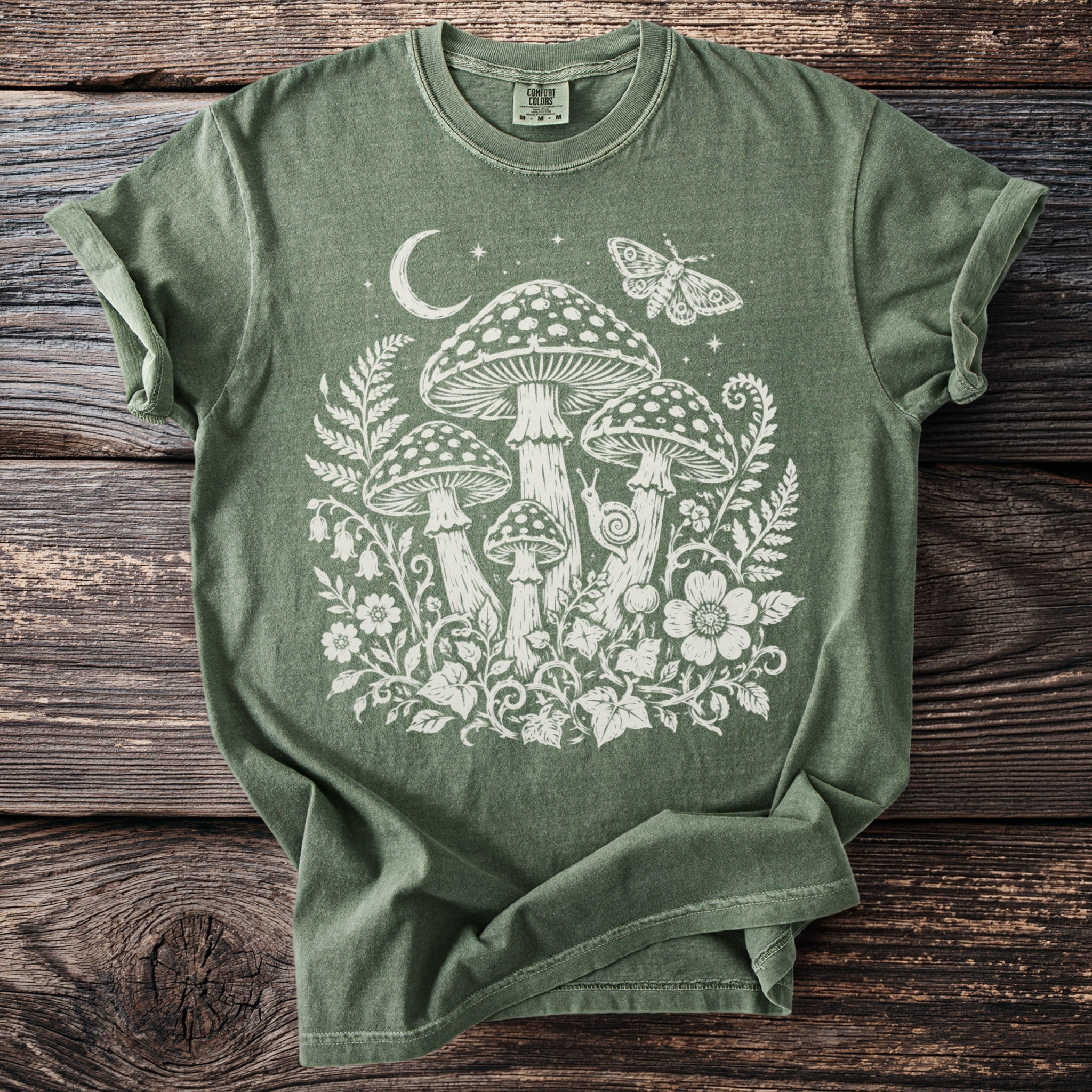 Olive green t-shirt with white mushroom, moon, moth, and floral design.