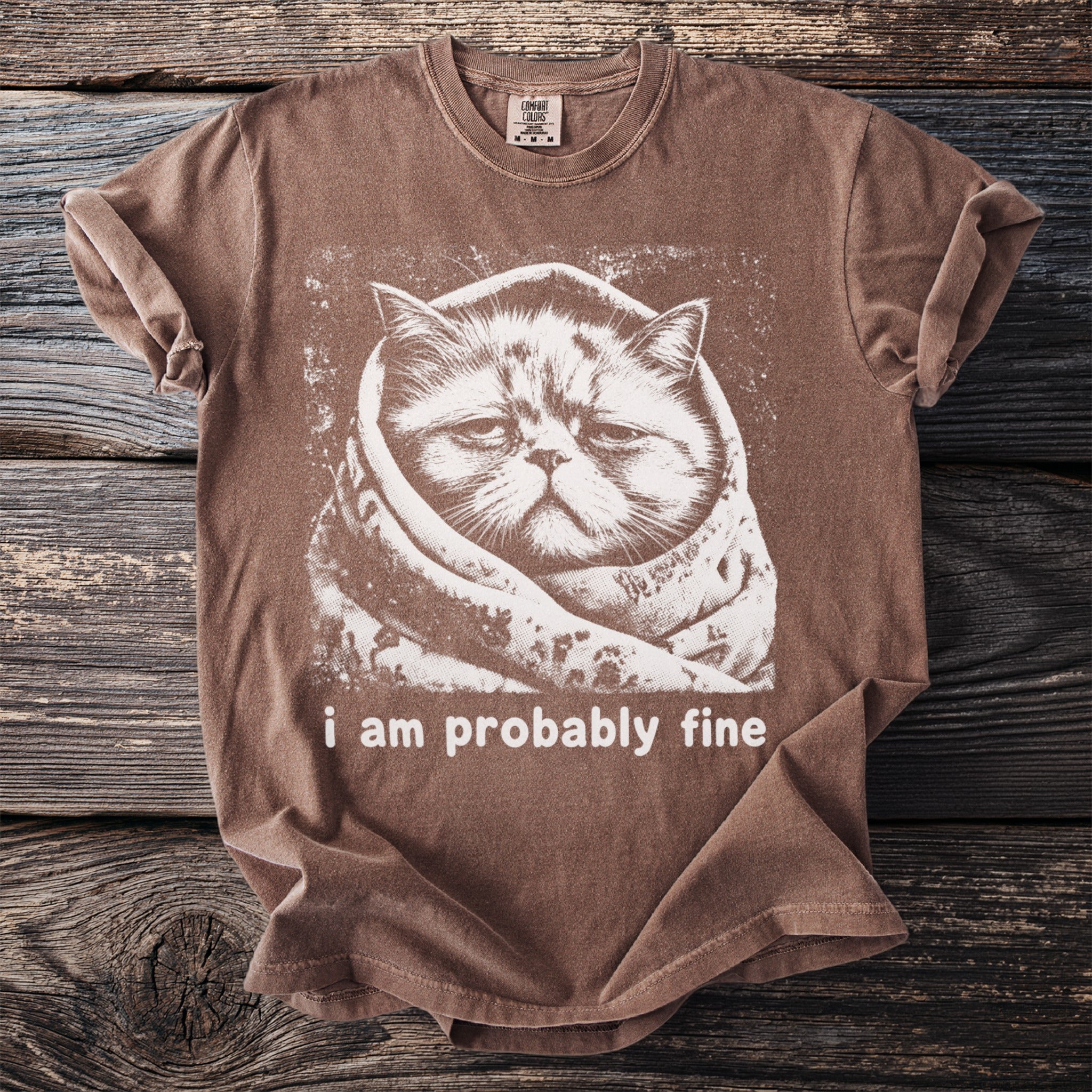 Brown t-shirt with a white graphic of a cat wrapped in a blanket, text reads "i am probably fine".