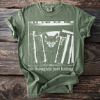 Green t-shirt with a graphic of a cat amongst books and the text "no thoughts just hiding".