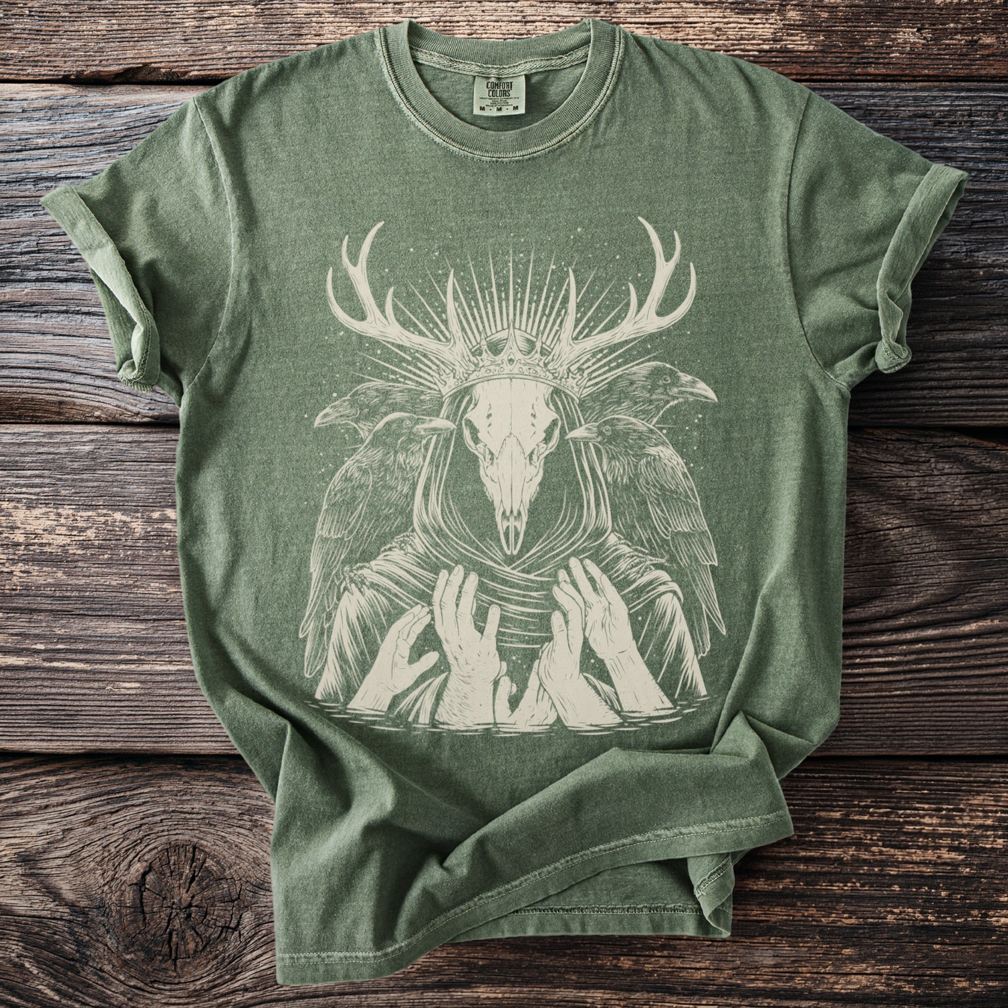 Green t-shirt with a light-colored graphic of a deer skull wearing a crown and surrounded by ravens.