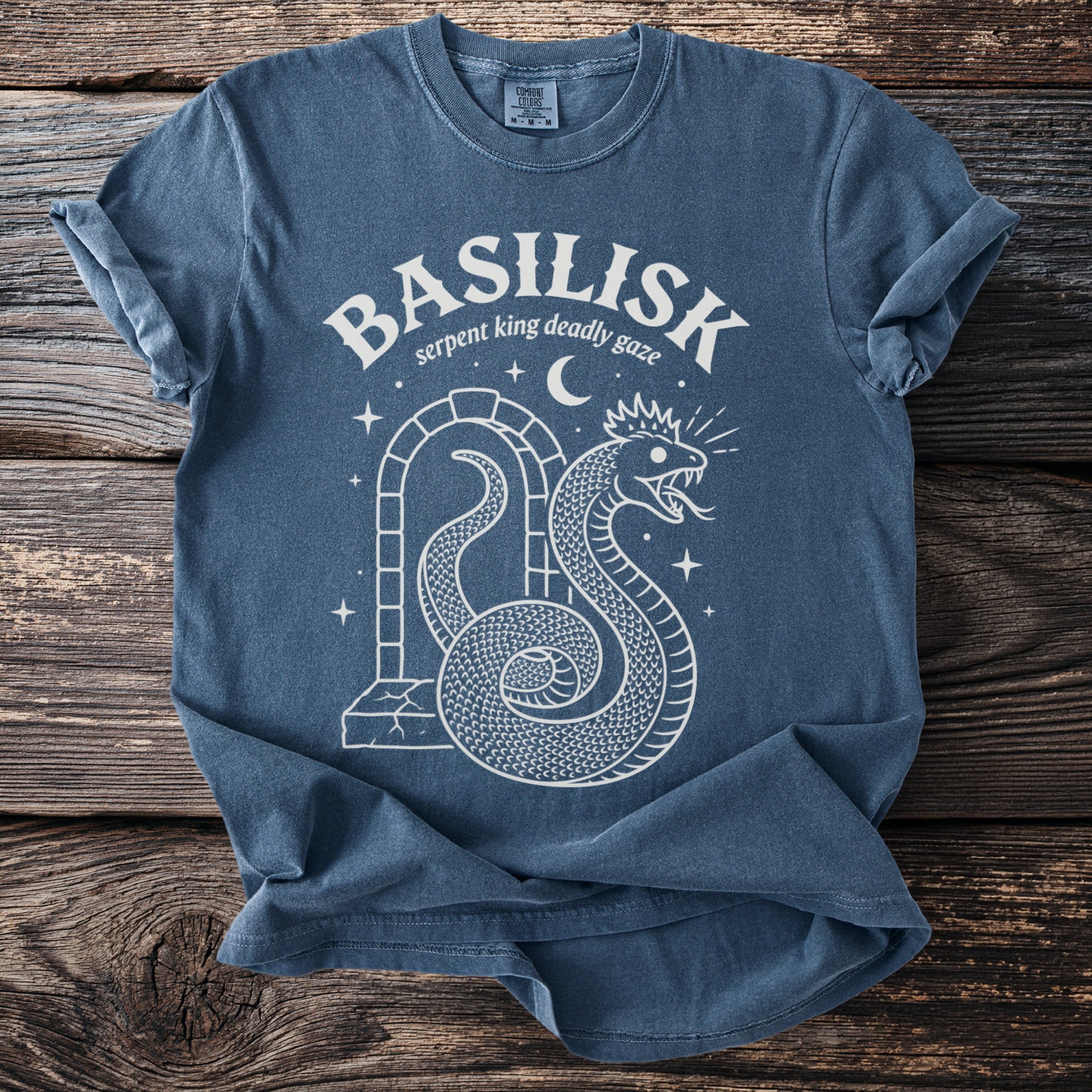 Blue t-shirt with white "BASILISK serpent king deadly gaze" text and snake graphic.