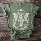 Olive green t-shirt with a light graphic of a praying woman with butterfly wings, moon phases, and mushrooms.