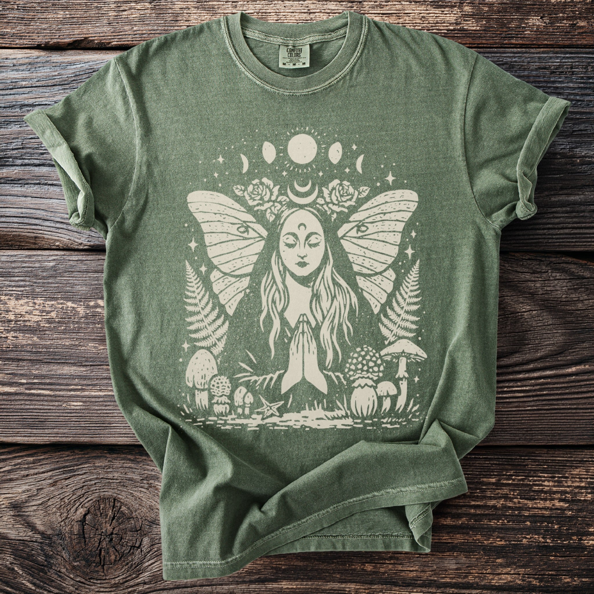 Olive green t-shirt with a light graphic of a praying woman with butterfly wings, moon phases, and mushrooms.