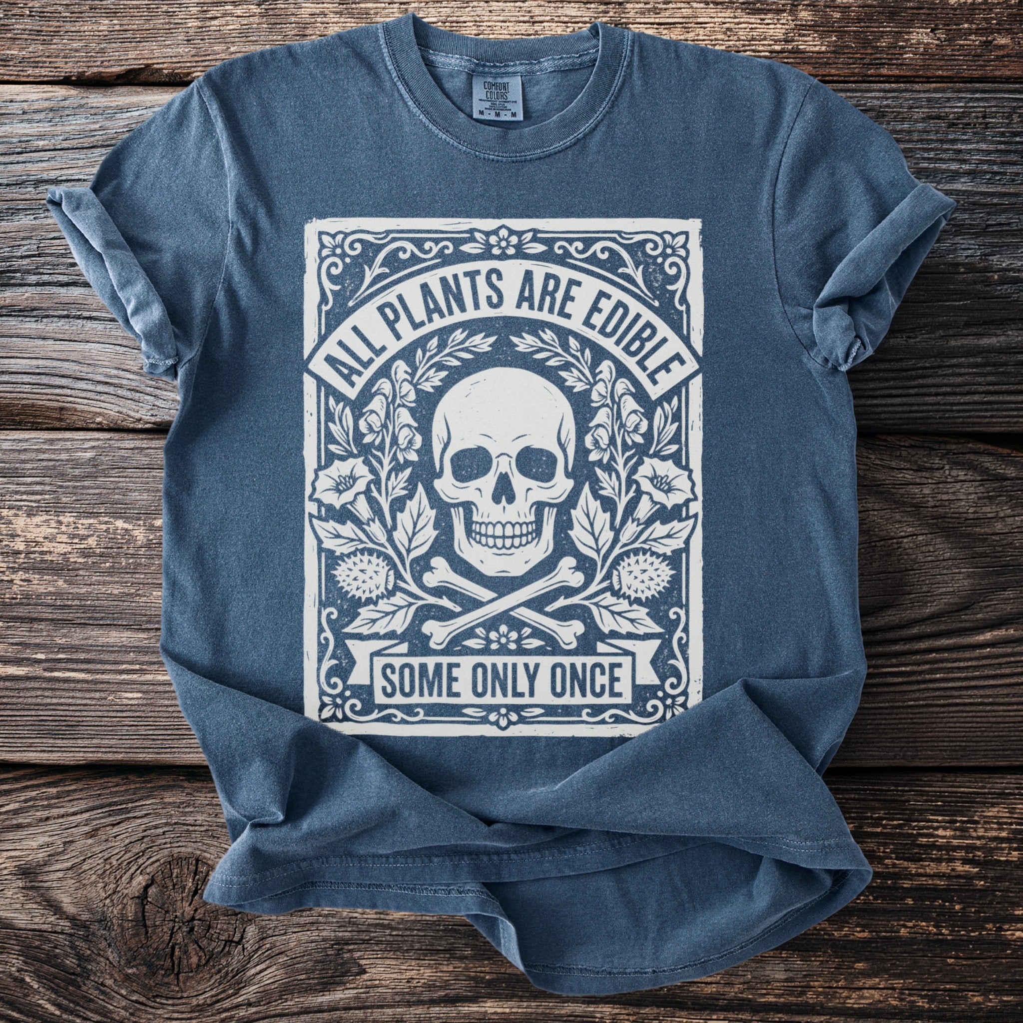 Blue t-shirt with skull, crossed bones, flowers, and text "ALL PLANTS ARE EDIBLE SOME ONLY ONCE".