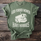 Green t-shirt with white text "God forbid women have hobbies" and coffin design.