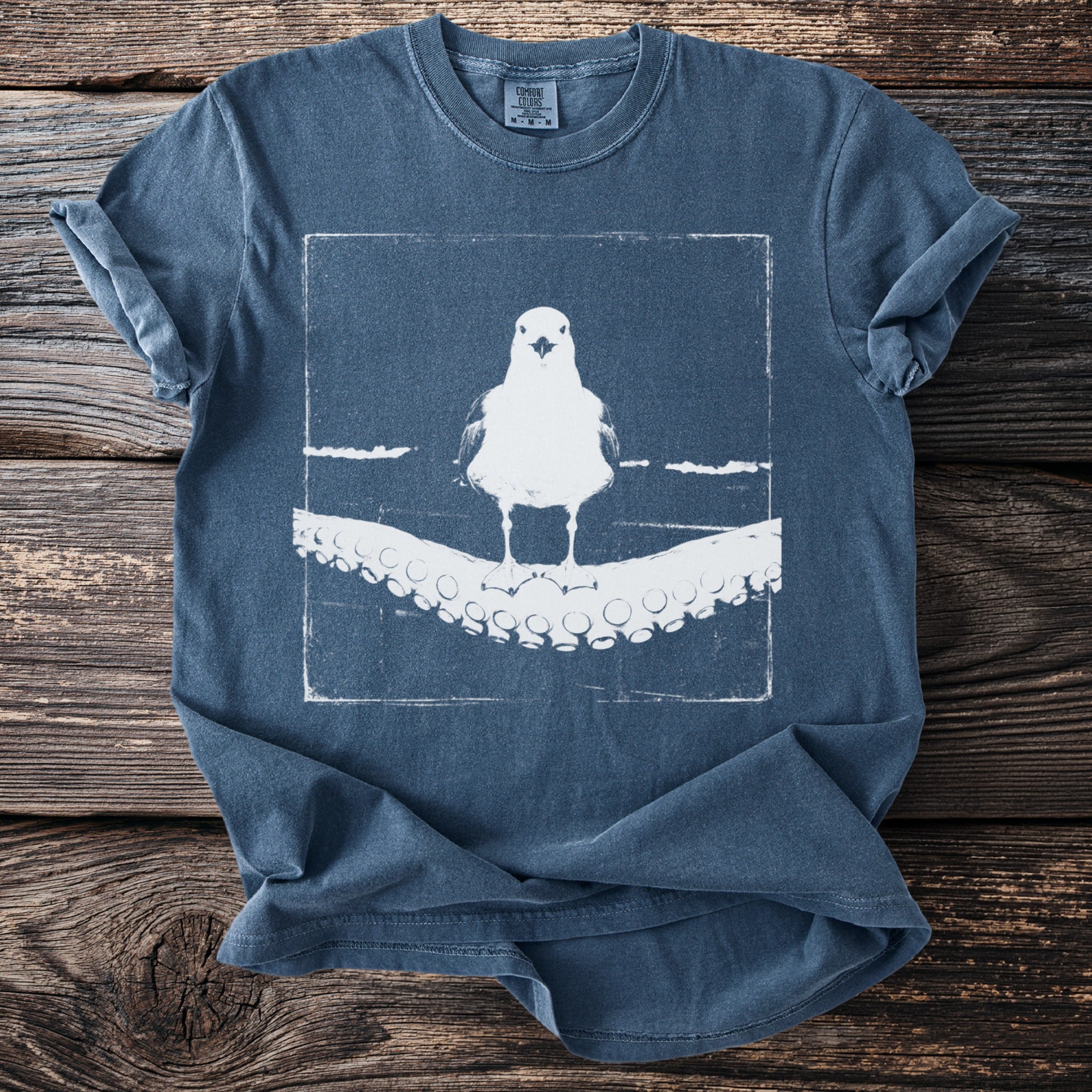 Blue t-shirt with a graphic of a seagull standing on an octopus tentacle.