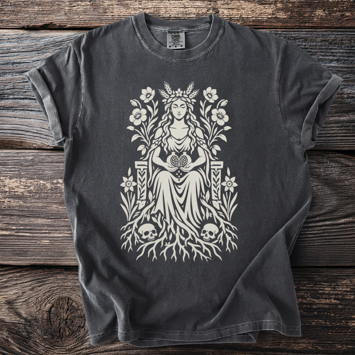 Dark gray t-shirt with a cream goddess illustration holding pomegranates, surrounded by flowers, roots, and skulls.
