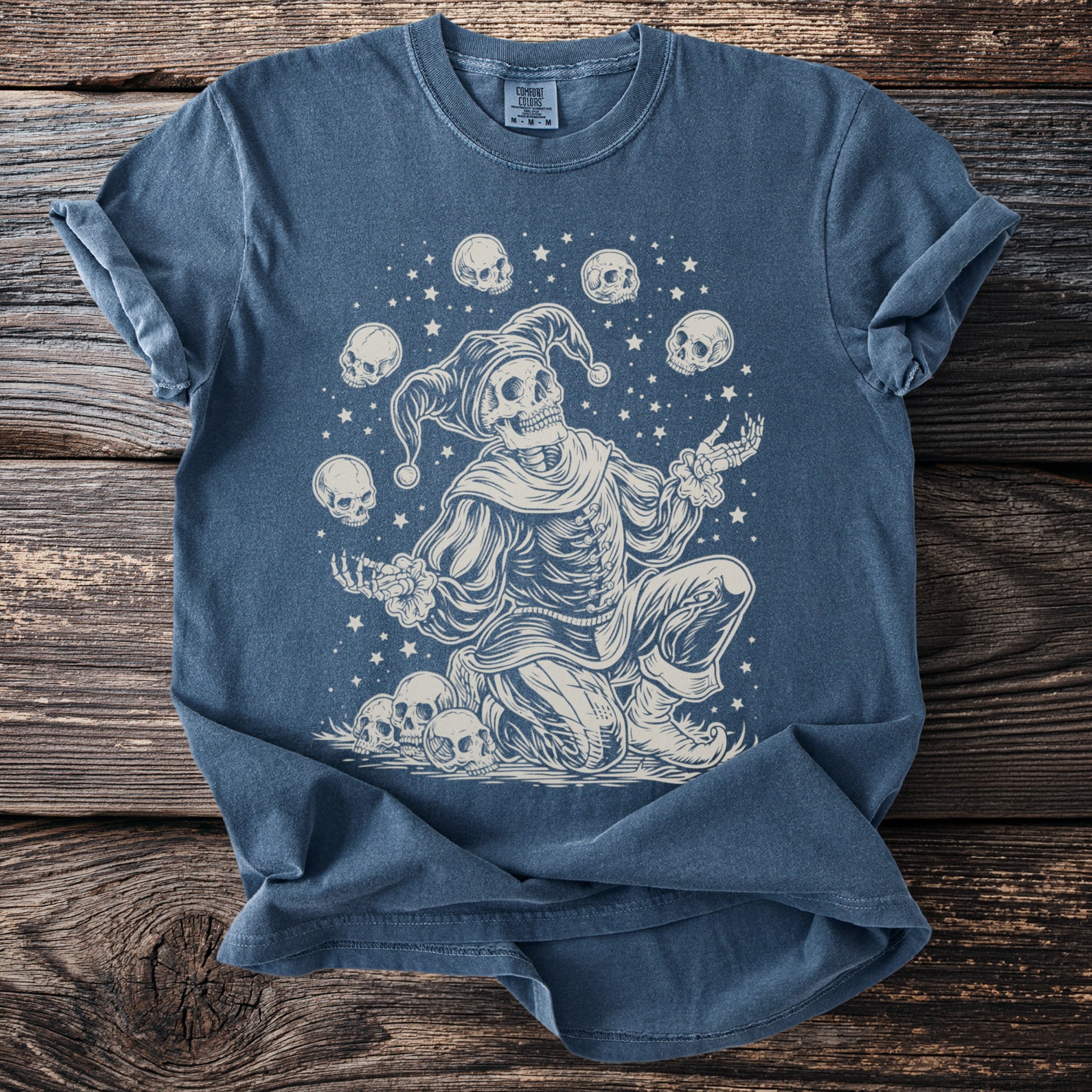 Skeleton jester juggling skulls with stars on a blue t-shirt.