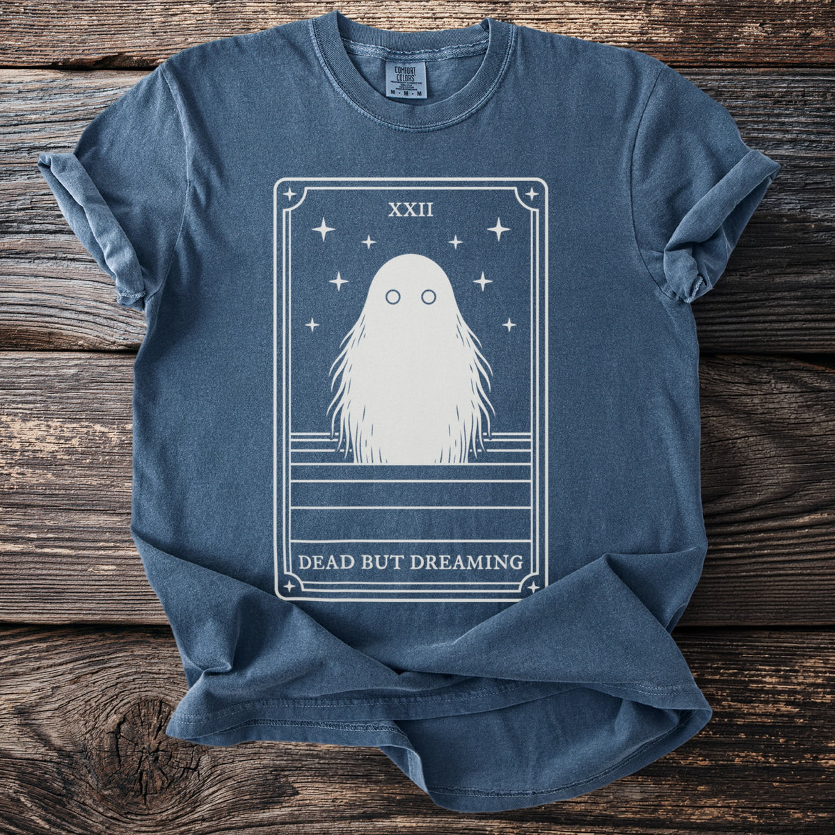 Blue t-shirt with tarot card design of a ghost and text "DEAD BUT DREAMING".