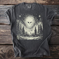 Dark gray t-shirt with an enormous grey face in the sky above a treeline, with a single small figure looking up from below.