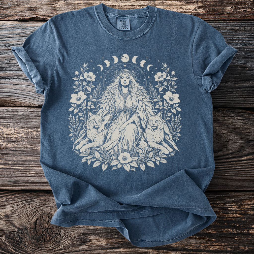Blue t-shirt with a central graphic of a woman with flowing hair, flanked by two cats, surrounded by floral elements and moon phases.