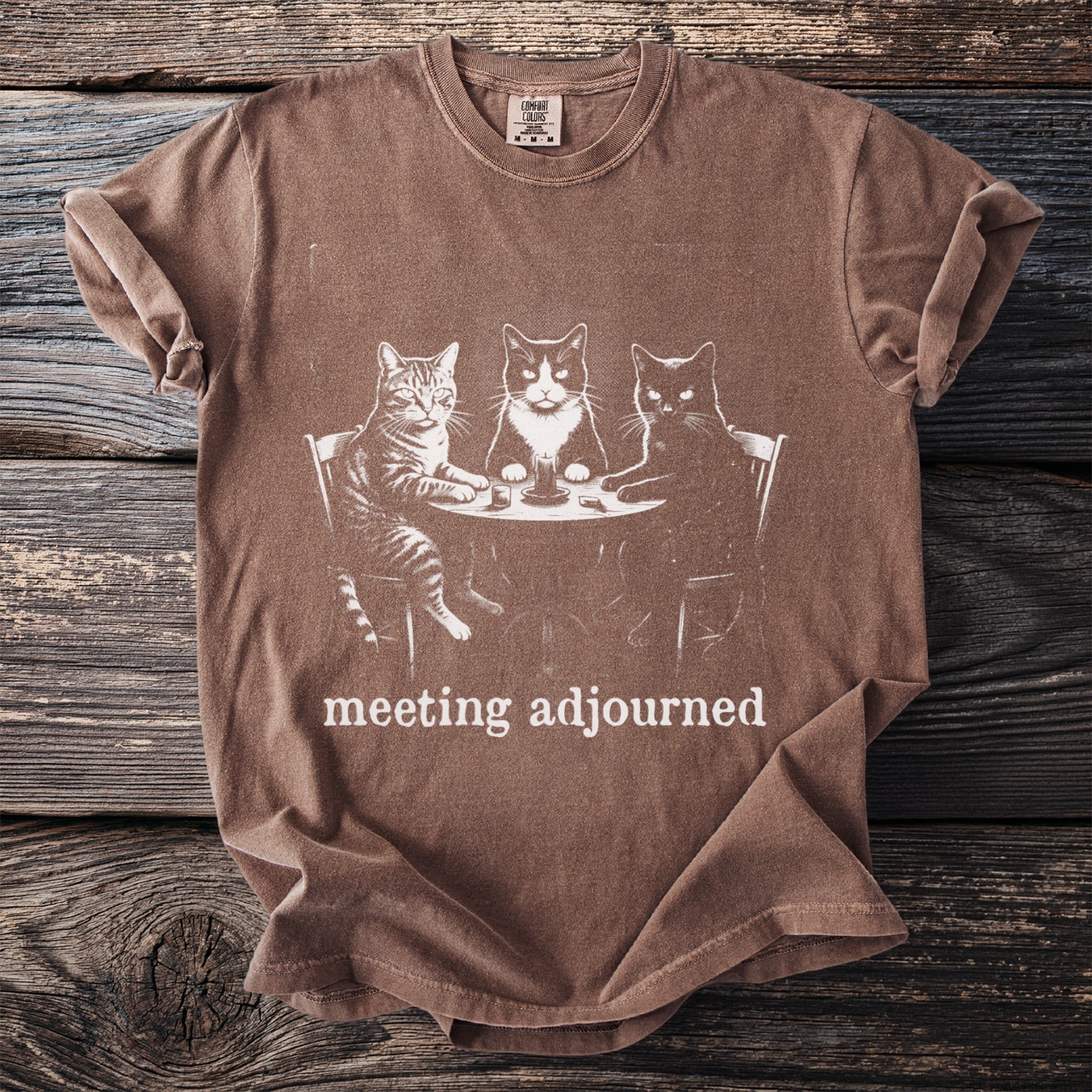 Brown t-shirt with a graphic of three cats sitting at a table, text reads "meeting adjourned".