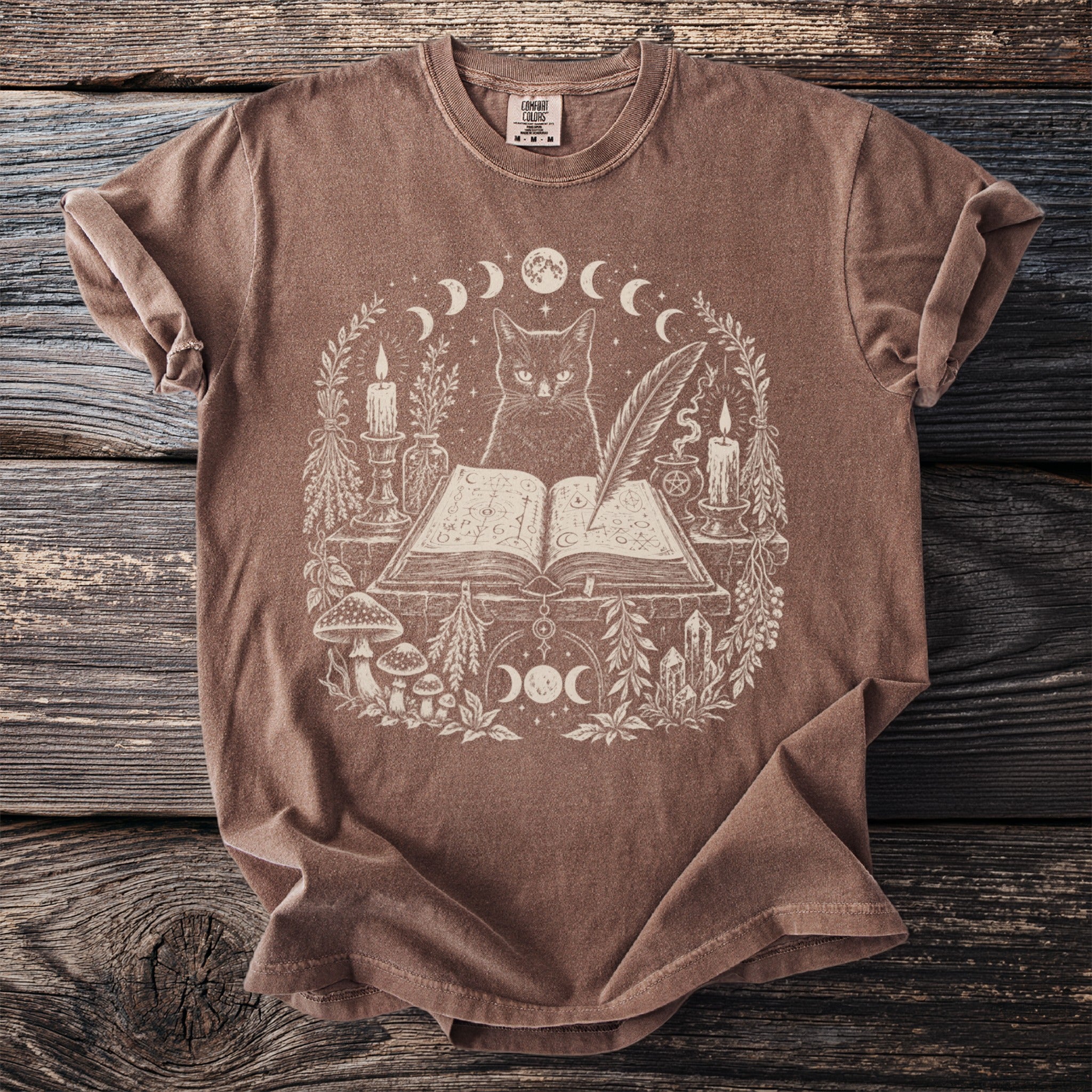 T-shirt with mystical cat, open book, candles, and celestial motifs in white print.