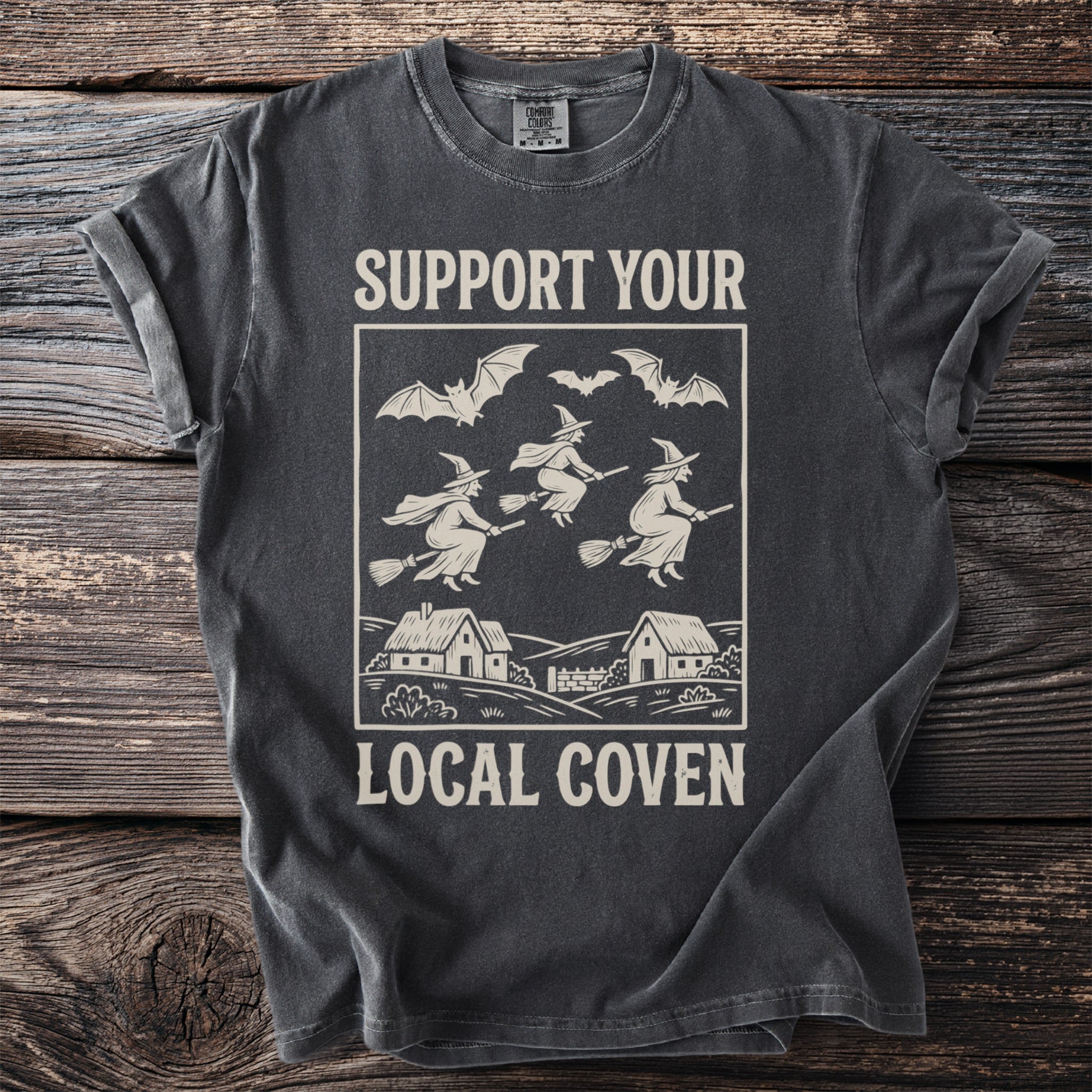 Dark grey t-shirt with graphic that says "Support Your Local Coven" featuring witches and bats.