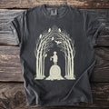 Dark gray t-shirt with a light beige graphic of a child holding a lantern on a rune stone among birches and owls.
