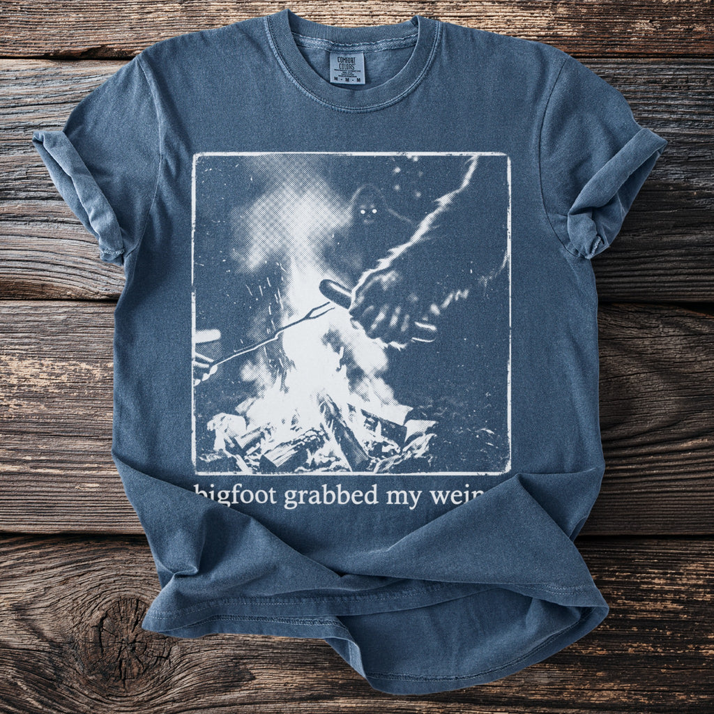 Blue t-shirt with a graphic of Bigfoot by a campfire and text "bigfoot grabbed my weir".