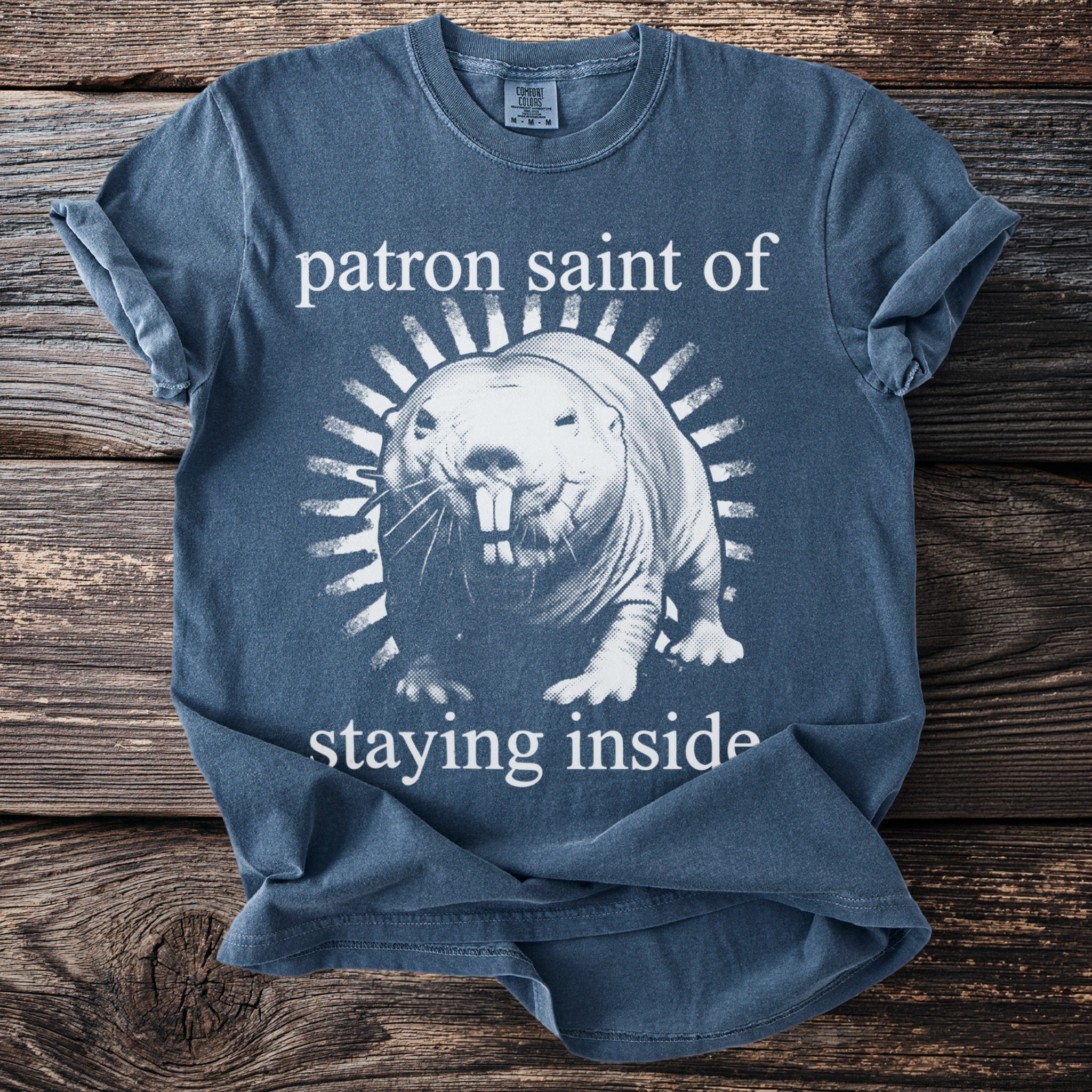 Blue t-shirt with a naked mole rat graphic and text "patron saint of staying inside".