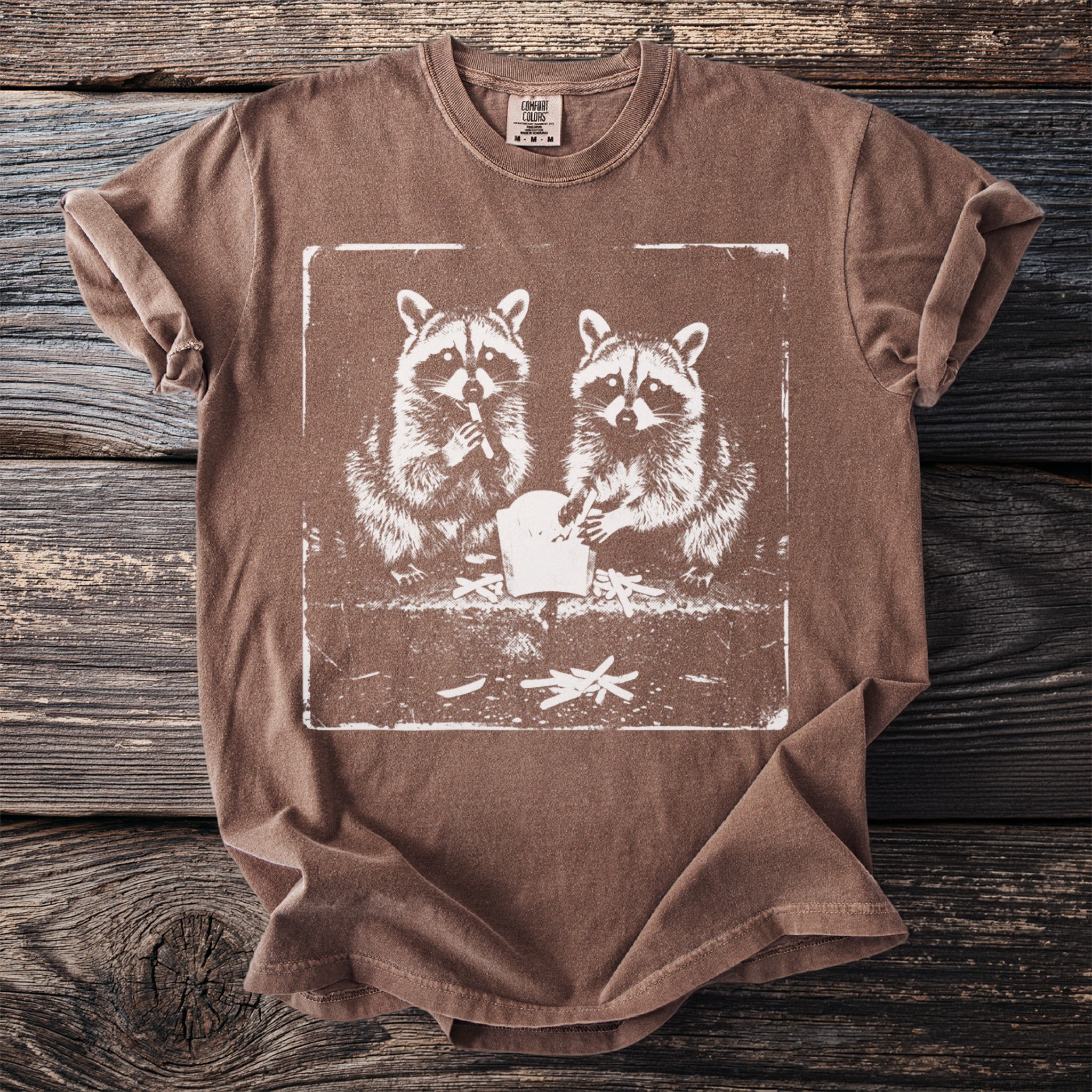 Brown t-shirt featuring a distressed graphic of two raccoons eating french fries.
