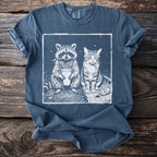 Graphic print of a raccoon holding a drink and a cat smoking on a blue t-shirt.