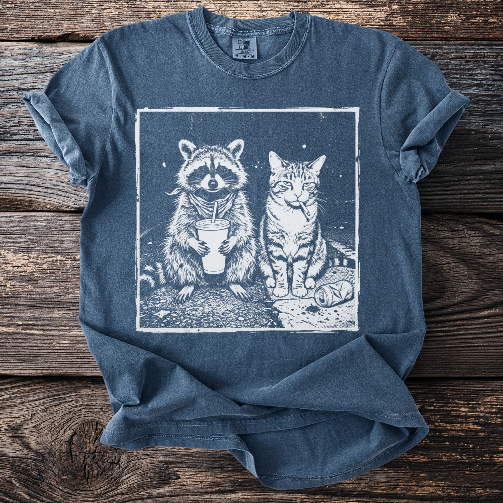 Graphic print of a raccoon holding a drink and a cat smoking on a blue t-shirt.