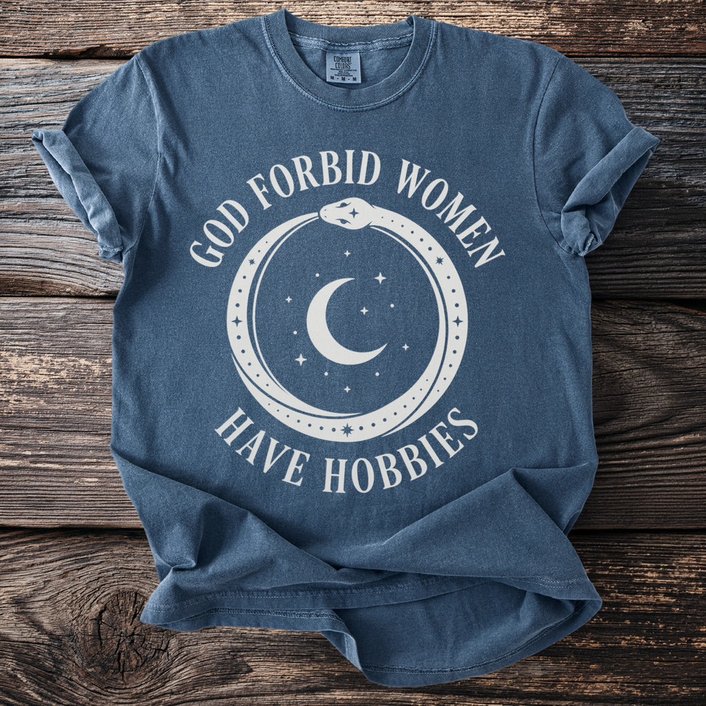 Blue t-shirt with white text "GOD FORBID WOMEN HAVE HOBBIES" and cosmic graphic.