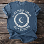 Blue t-shirt with white text "GOD FORBID WOMEN HAVE HOBBIES" and cosmic graphic.