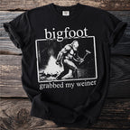 Black t-shirt with Bigfoot by a campfire holding a hot dog.