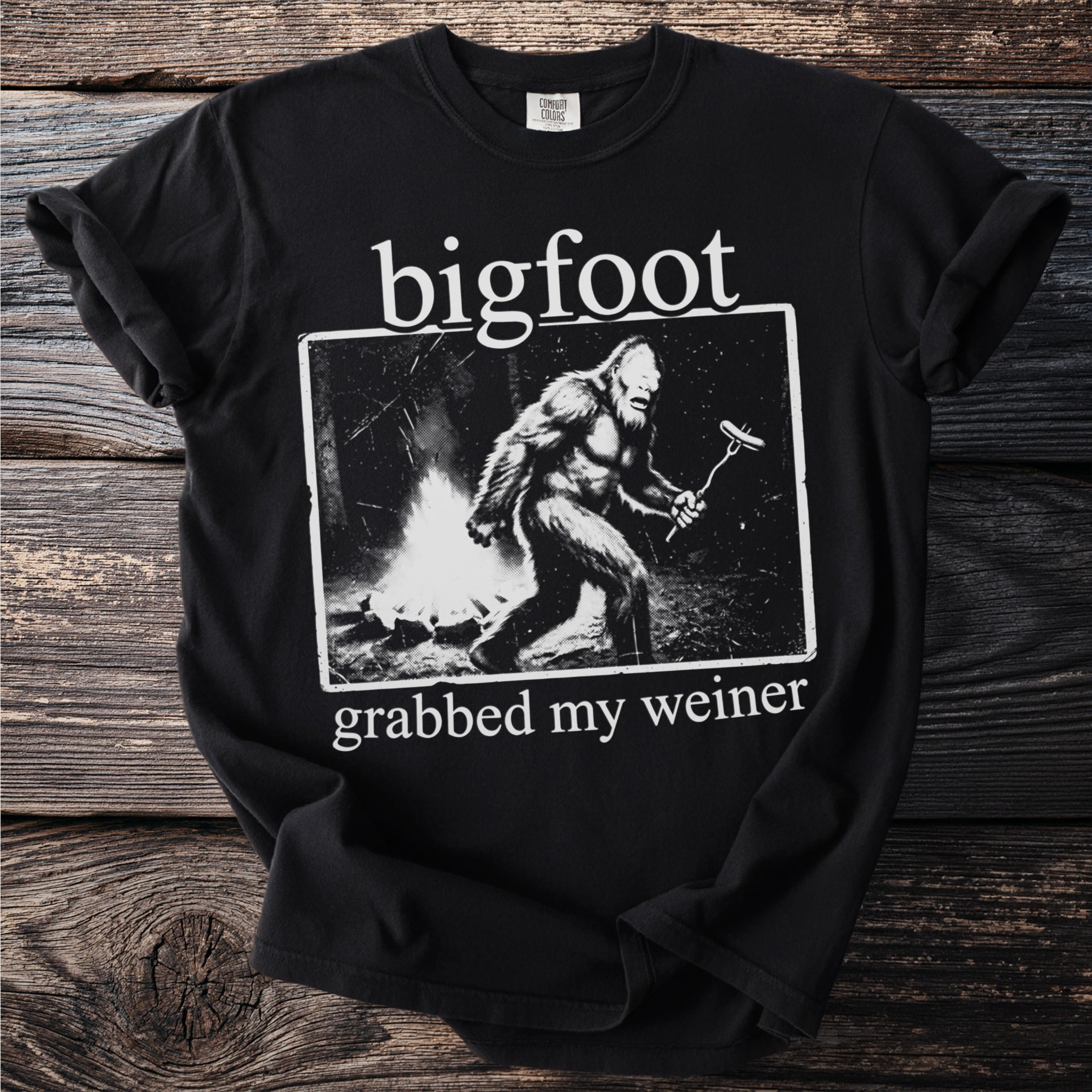 Black t-shirt with Bigfoot by a campfire holding a hot dog.