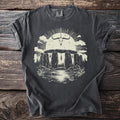 Dark t-shirt with cream graphic of Stonehenge, a bull skull, and wolves by a lake.