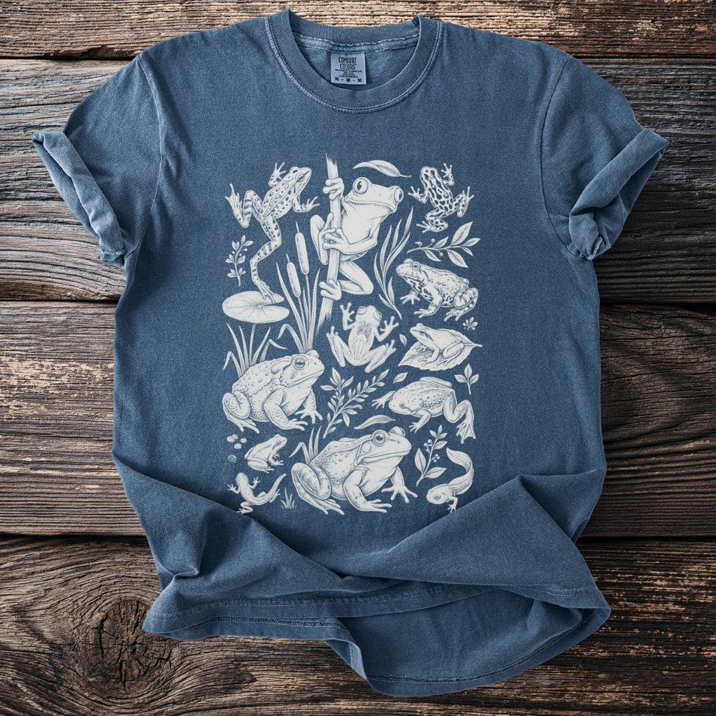 Blue t-shirt with white line art illustration of various frogs and tadpoles.