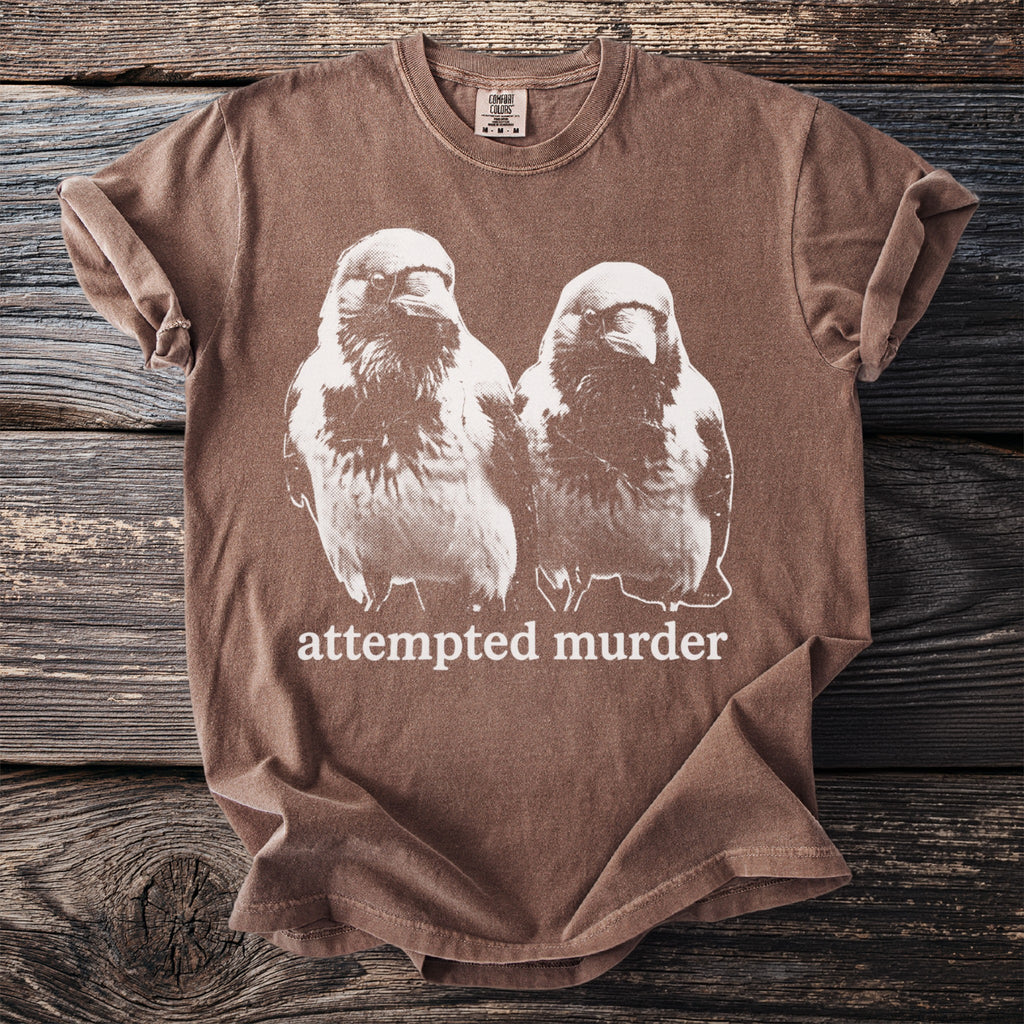 Brown t-shirt with white graphic of two birds and text "attempted murder".