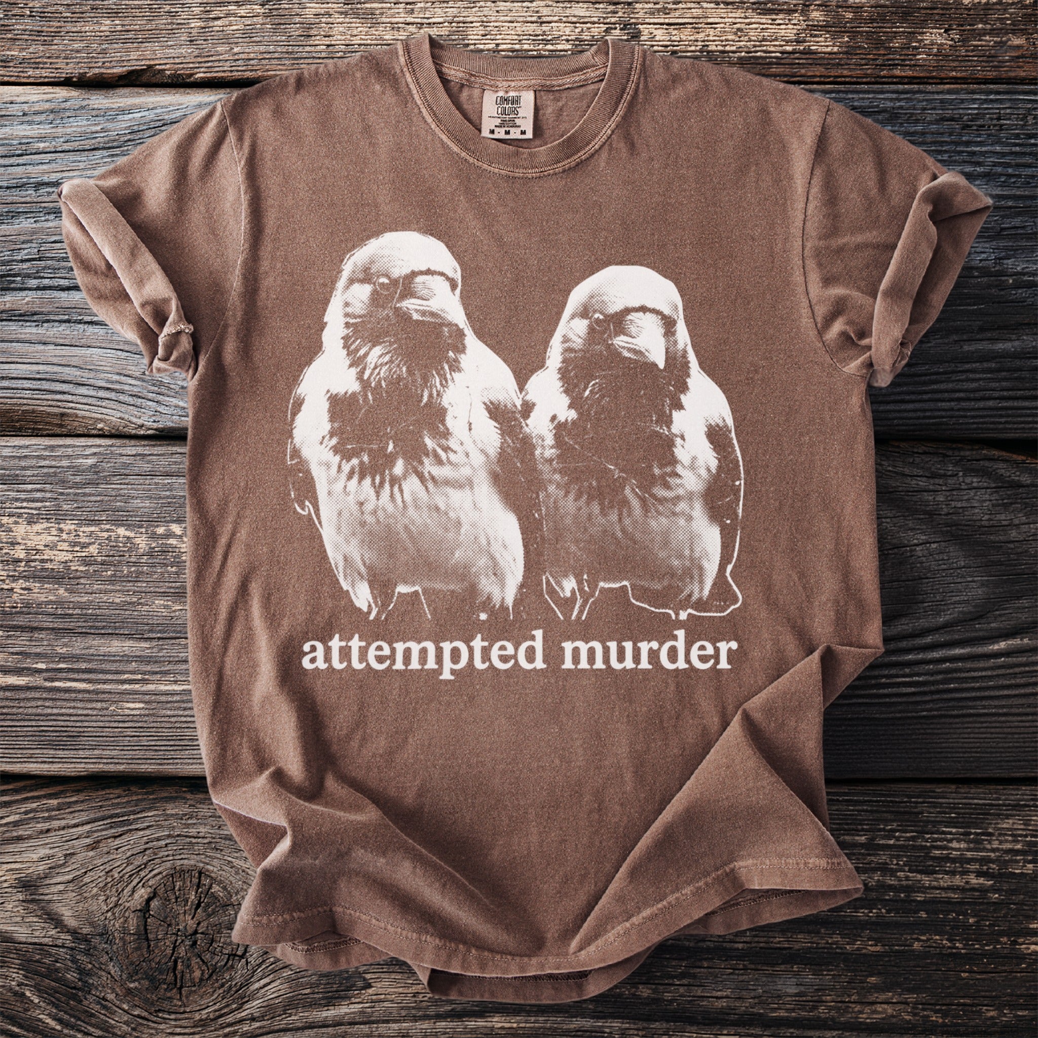 Brown t-shirt with white graphic of two birds and text "attempted murder".