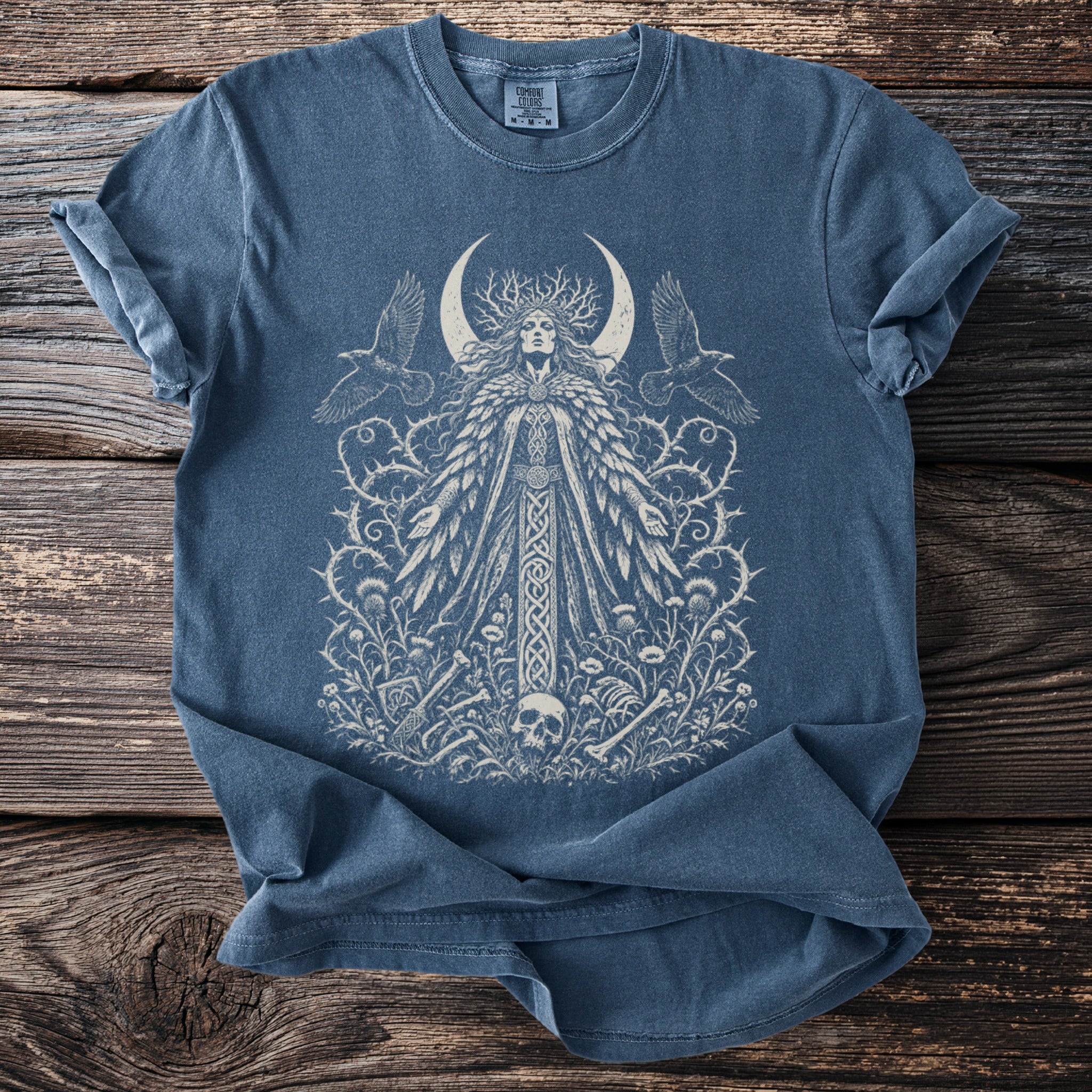 Blue t-shirt with a white intricate design of a moon goddess, birds, and thorny vines.