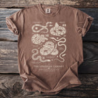 Brown t-shirt with detailed illustrations and text of various snakes and "The Ophidian Cabinet" title.