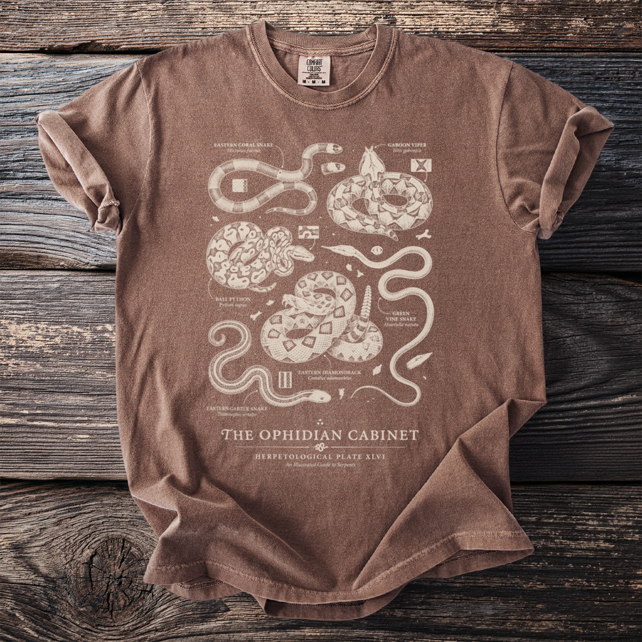 Brown t-shirt with detailed illustrations and text of various snakes and "The Ophidian Cabinet" title.