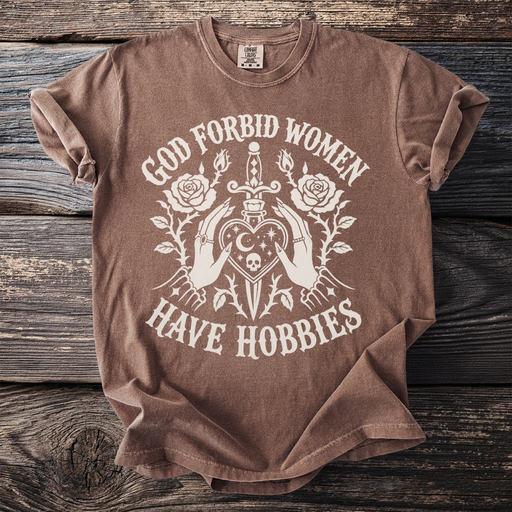 Brown t-shirt with white graphic design and text that reads "God forbid women have hobbies".